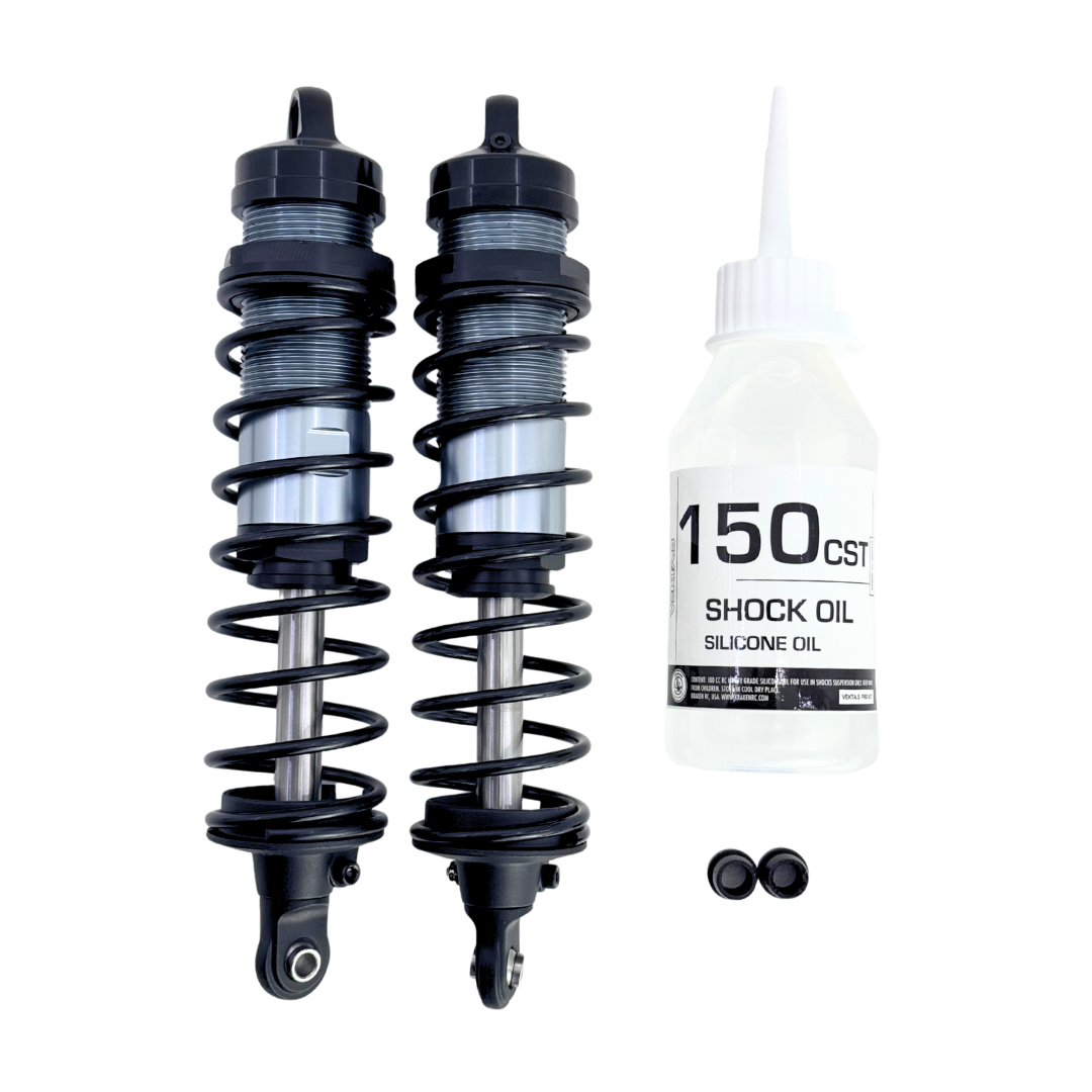 Two shock absorbers and a bottle of shock oil on a white background