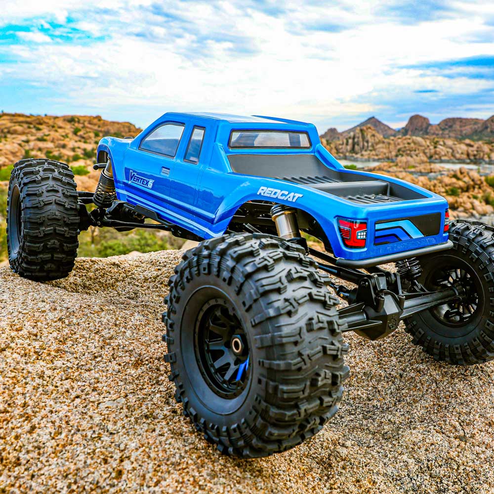 Blue remote control truck with large wheels on a sandy surface with desert landscape in the background