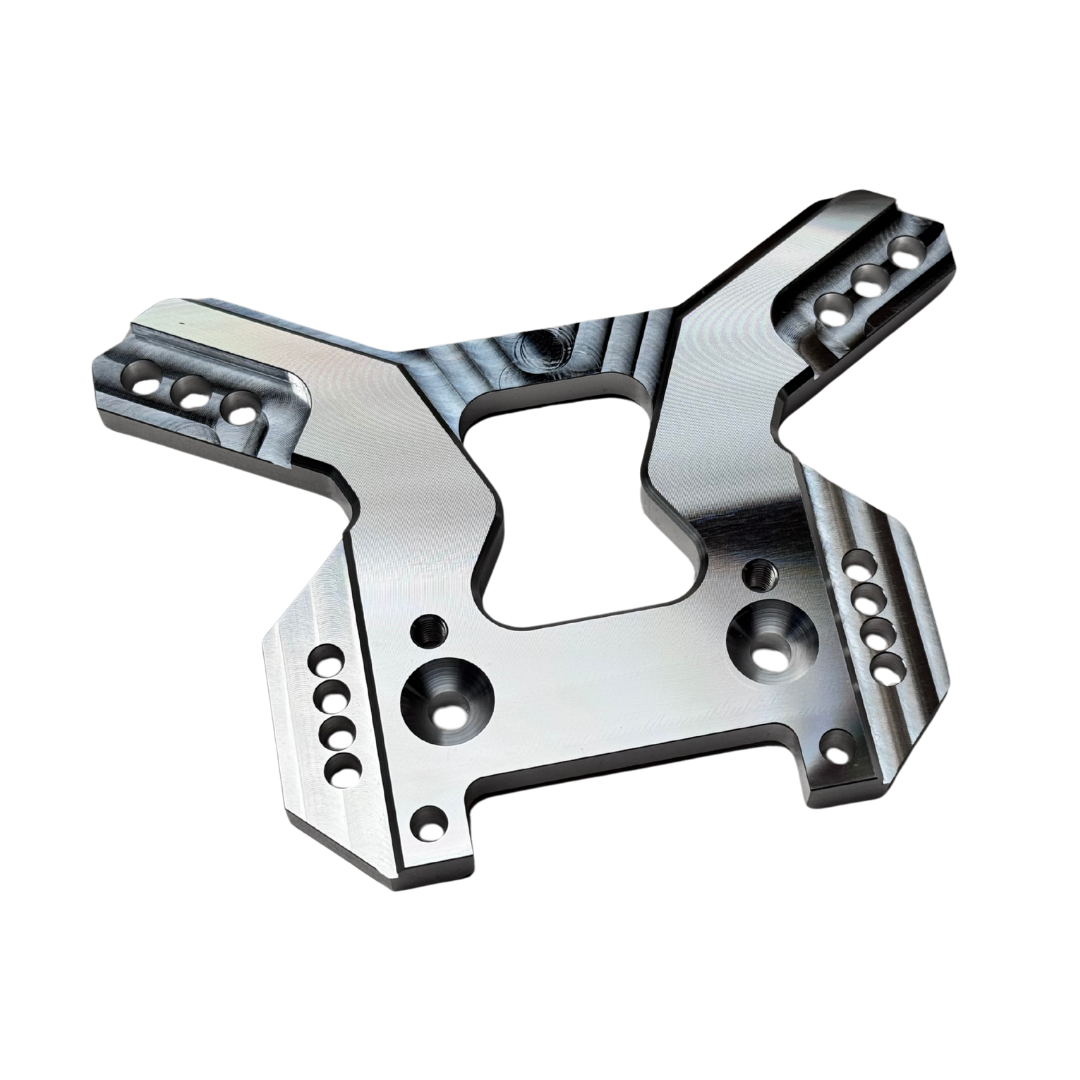 Taylor RC OUTLAW V4 front shock tower in raw silver, angled view showing the shock mounting holes, arm slots, and central chassis clearance cutout