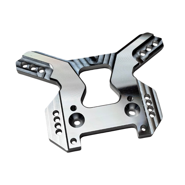 Taylor RC OUTLAW V4 front shock tower in raw silver, angled view showing the shock mounting holes, arm slots, and central chassis clearance cutout
