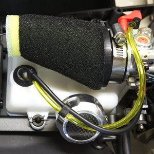 A black foam air filter for a vehicle, installed within the engine compartment, showing the filter material and the yellow fuel lines.