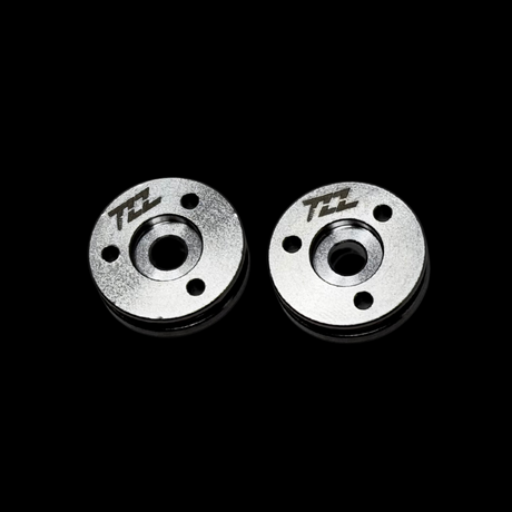 Two metal MCD shock pistons with TZZ logo on a black background